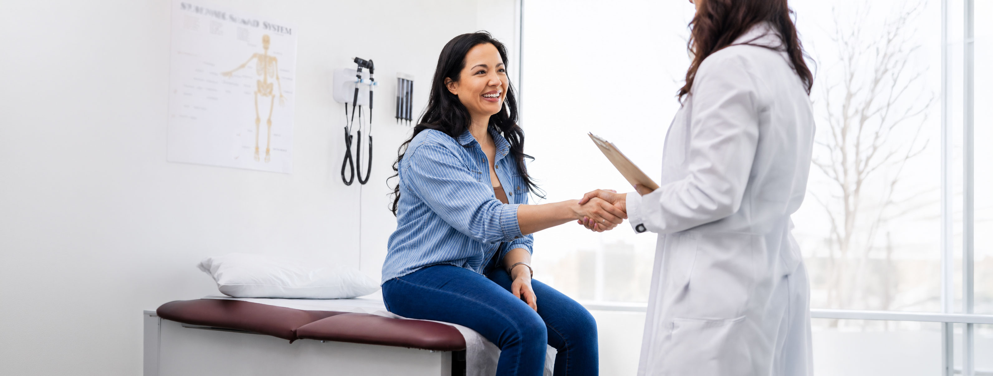 A smiling patient shaking hands with her doctor in a bright exam room
